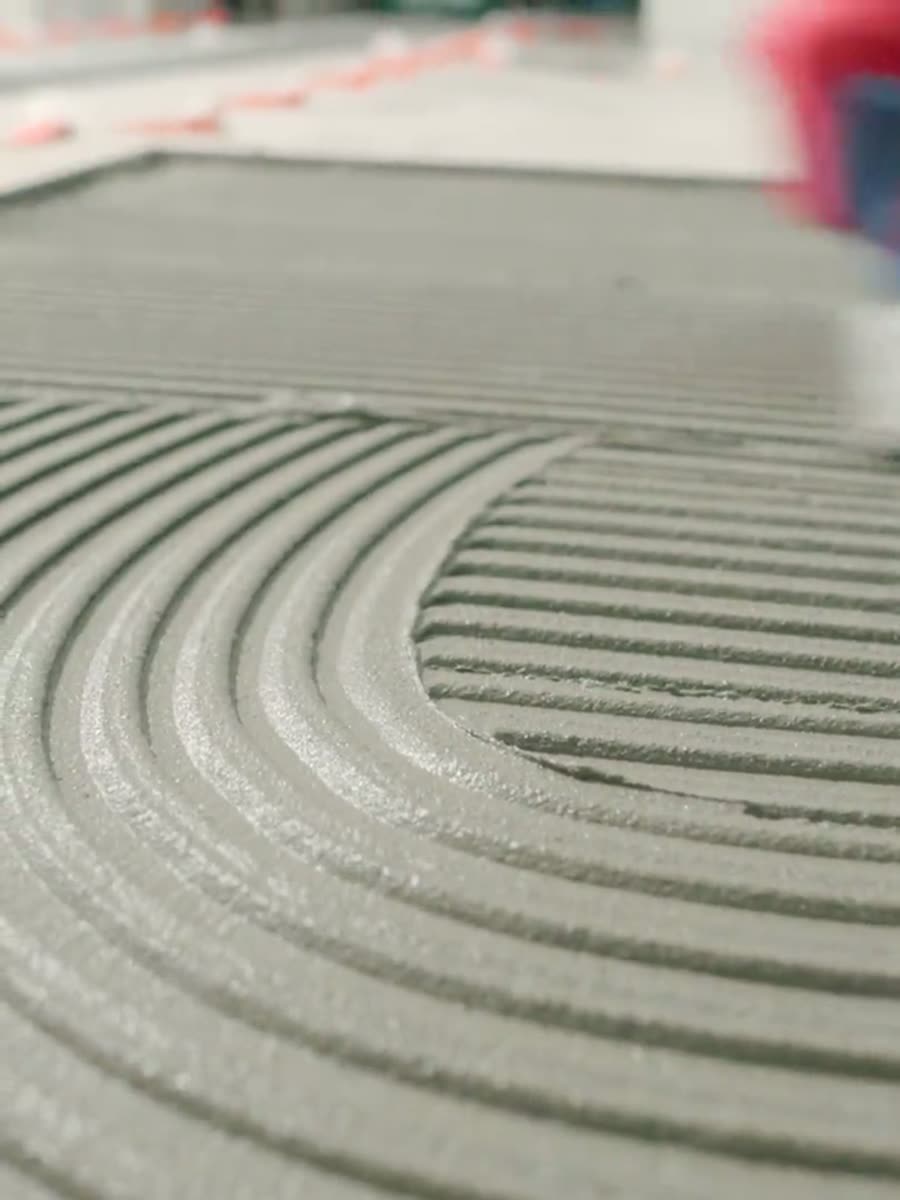 Combed adhesive ridges across a floor with tile spacers waiting behind