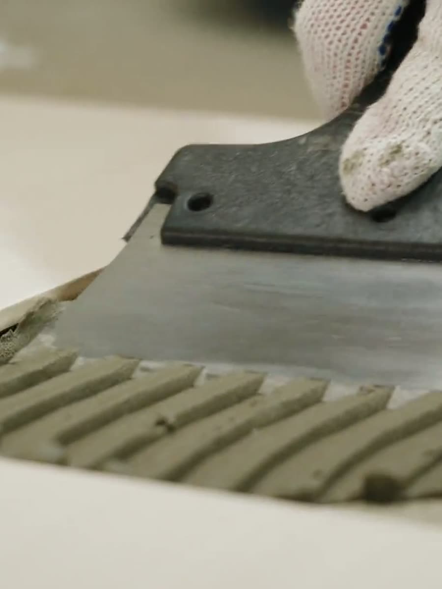 Gloved hand drawing a notched trowel through adhesive, leaving even ridges