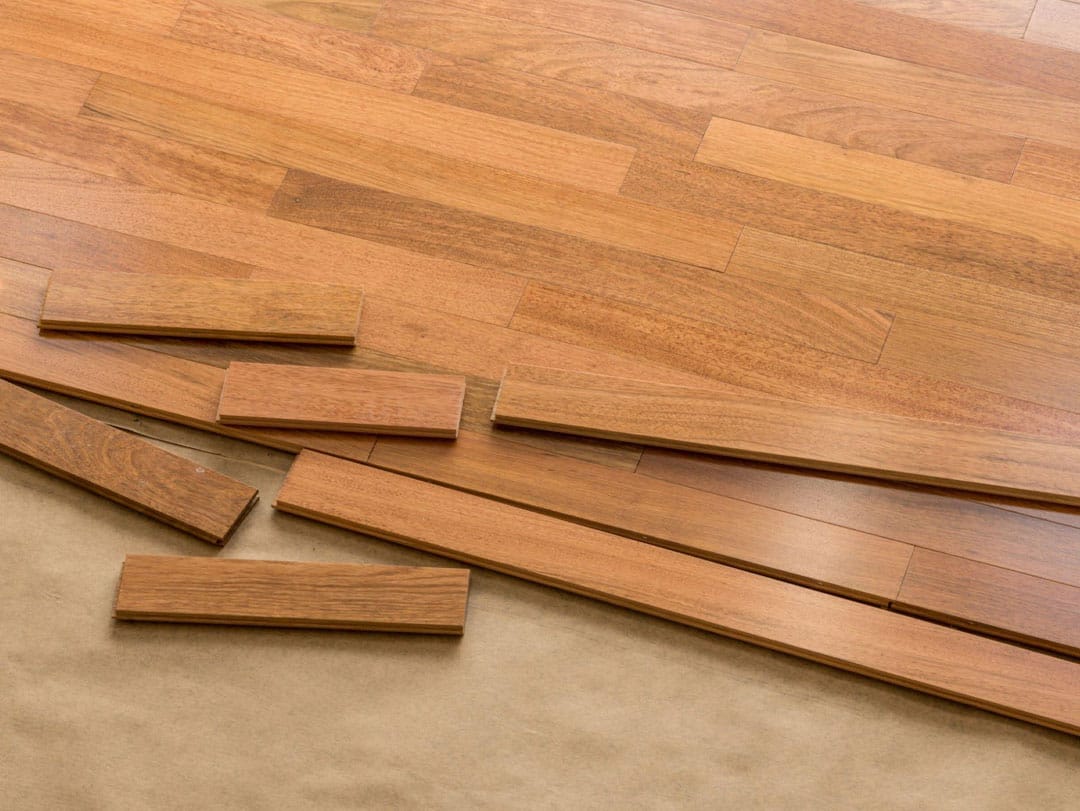 Wooden flooring planks being installed over existing floor with loose pieces scattered around